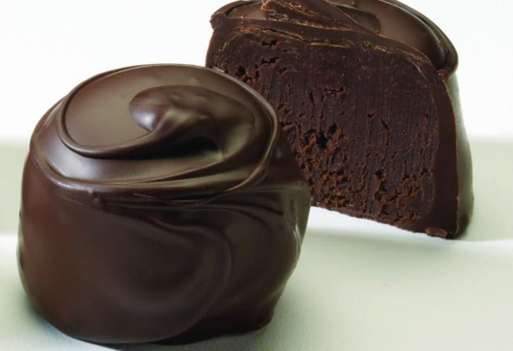 An image of a chocolate truffle, with one whole and one cut in half to show the cherry center, on a white background.