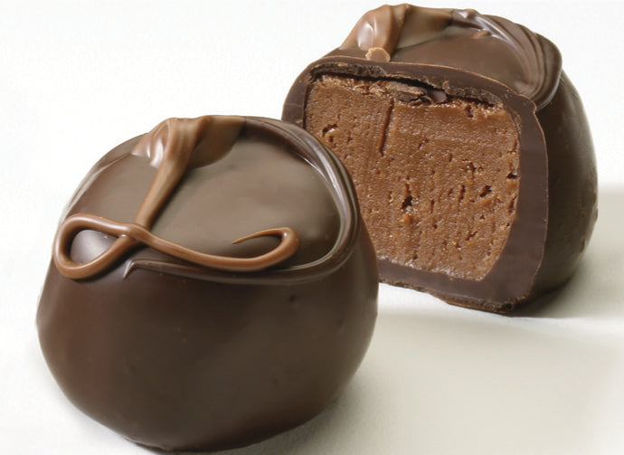 An image showing two dark chocolate truffles, one whole and one cut in half to reveal the milk chocolate center.