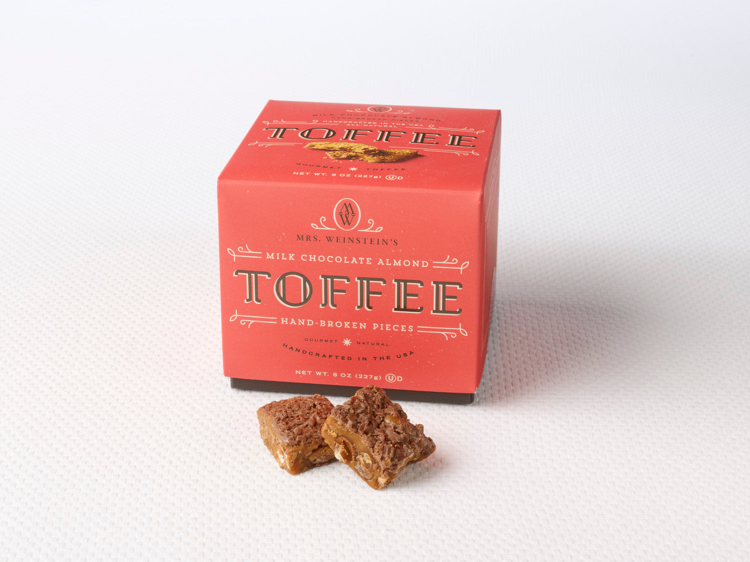 A box of Milk Chocolate Almond Toffee Squares with some pieces of toffee placed in front of the box. Sweet Shop USA Mrs Weinsteins Toffee