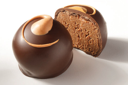 A chocolate covered truffle with a milk chocolate swirl on top, cut in half to show the dark chocolate layer and the milk chocolate topping.